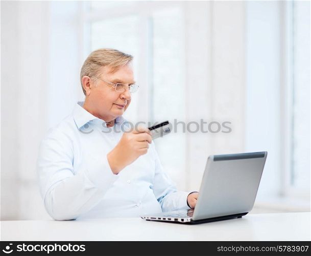 business, online banking, internet shopping and oldness concept - smiling old man with laptop computer and credit card at home
