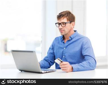 business, online banking, internet shopping concept - smiling man with laptop and credit card at home