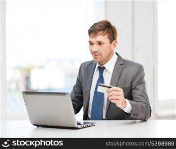 business, online banking, internet shopping concept - smiling man with laptop and credit card in office