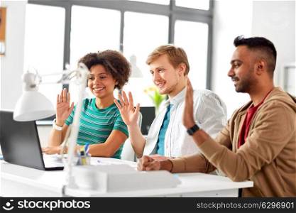 business, online communication and technology concept - happy creative team having video conference or interview at office and waving hands. creative team having video conference at office. creative team having video conference at office