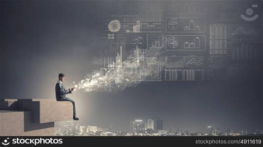 Business online. Young businessman sitting on building top with mobile phone in hand