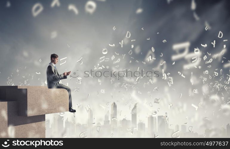 Business online. Young businessman sitting on building top with mobile phone in hand