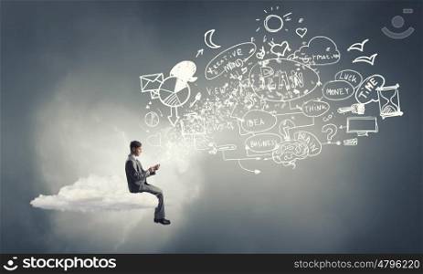 Business online. Young businessman sitting on cloud with mobile phone in hands