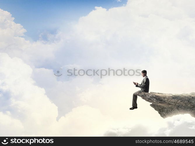 Business online. Young businessman sitting on rock edge with mobile phone in hand