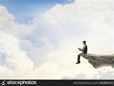 Business online. Young businessman sitting on rock edge with mobile phone in hand