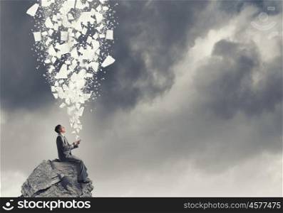 Business online. Young businessman sitting on rock top with mobile phone in hand