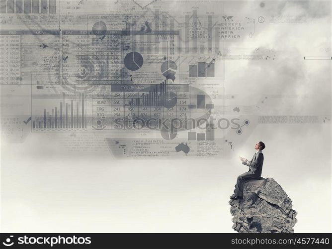 Business online. Young businessman sitting on top of rock with mobile phone in hand