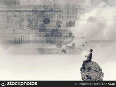 Business online. Young businessman sitting on top of rock with mobile phone in hand