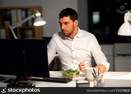 business, overwork, deadline and people concept - businessman at computer eating vegetable salad at night office. businessman at computer eating at night office