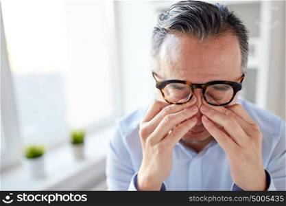 business, overwork, deadline and people concept - close up of tired businessman in eyeglasses rubbing eyes at office. businessman in glasses rubbing eyes at office