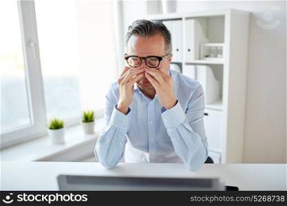 business, overwork, deadline and people concept - tired businessman in eyeglasses with laptop computer rubbing eyes at office. tired businessman in glasses with laptop at office
