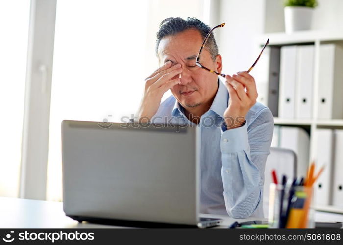 business, overwork, deadline and people concept - tired businessman with eyeglasses and laptop computer rubbing eyes at office. tired businessman with glasses at laptop in office