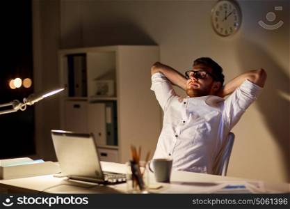 business, overwork, deadline and people concept - tired man with laptop working at night office and stretching. man with laptop stretching at night office