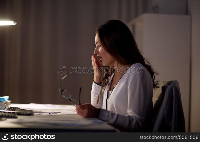 business, overwork, deadline and people concept - tired woman with eyeglasses yawning at night office. tired woman with glasses yawning at night office