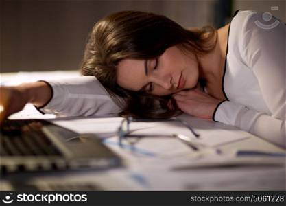 business, overwork, deadline and people concept - tired woman with laptop and papers sleeping on table at night office. tired woman sleeping on office table at night