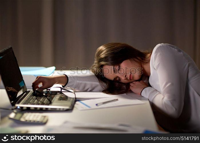 business, overwork, deadline and people concept - tired woman with laptop and papers sleeping on table at night office. tired woman sleeping on office table at night