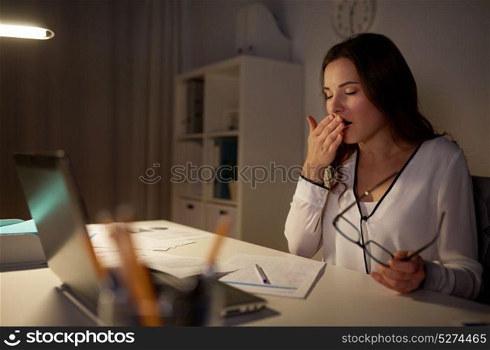 business, overwork, deadline and people concept - tired woman with papers and laptop yawning at night office. tired woman with papers yawning at night office