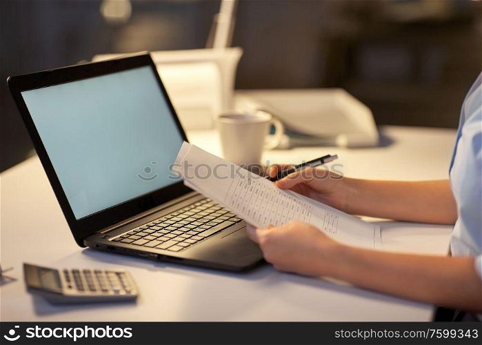 business, overwork, deadline and people concept - woman with laptop and papers working at dark night office. woman with laptop and papers at night office