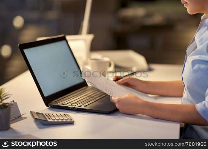 business, overwork, deadline and people concept - woman with laptop and papers working at dark night office. woman with laptop and papers at night office