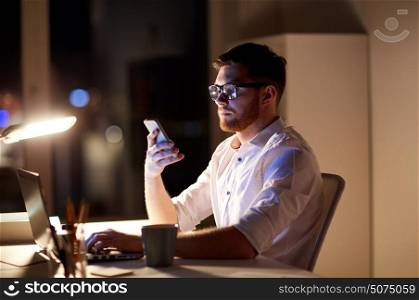 business, overwork, people, deadline and technology concept - businessman in glasses with laptop computer texting on smartphone at night office. businessman texting on smartphone at night office