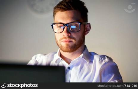 business, overwork, people, deadline and technology concept - businessman in glasses with laptop computer thinking at night office. businessman in glasses with laptop at night office