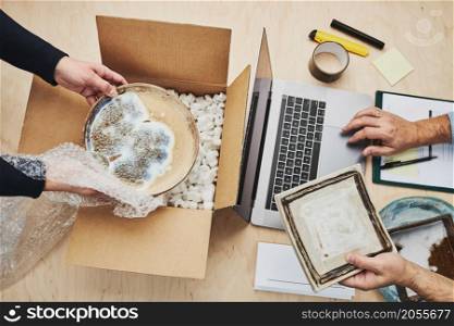 Business owner packing online order to delivery to customer. Preparing parcel box with ceramic plate product from online shop