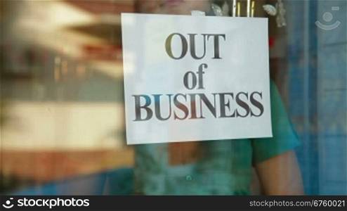 Business owner puts up Out Of Business sign on door of her store, closeup