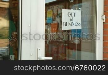 Business owner puts up Out Of Business sign on door of her store, medium shot