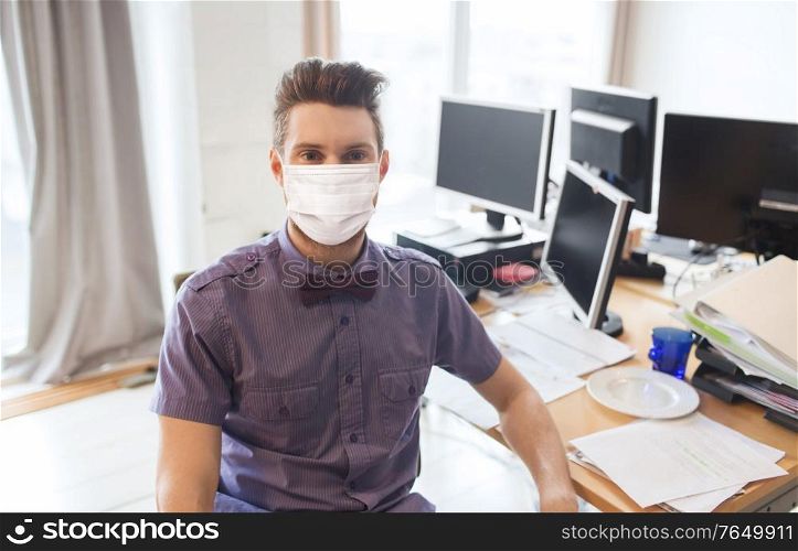 business, pandemic and health concept - businessman or creative male office worker wearing face protective medical mask for protection from virus disease with computers. male office worker in mask with computers
