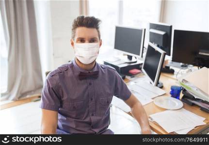 business, pandemic and health concept - businessman or creative male office worker wearing face protective medical mask for protection from virus disease with computers. male office worker in mask with computers