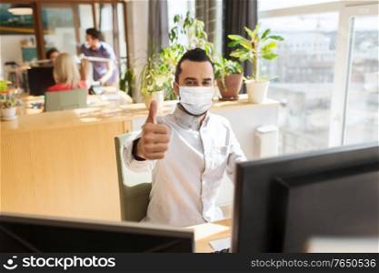 business, pandemic and health concept - businessman or creative male office worker wearing face protective medical mask for protection from virus disease with computer showing thumbs up. male office worker in mask showing thumbs up
