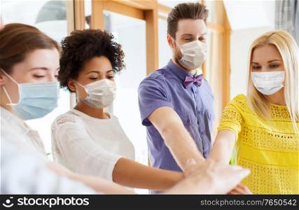 business, pandemic and health concept - creative team wearing face protective medical masks for protection from virus disease stacking hands at office. people in masks stacking hands at office