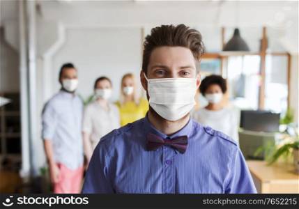 business, pandemic and health concept - young man wearing face protective medical mask for protection from virus disease with beard over creative team in office. young man in mask over creative team at office