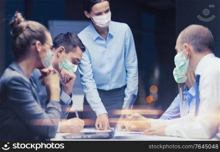 business, pandemic and people concept - female boss wearing face protective medical mask for protection from virus disease working with team at night office. female boss in mask with business team at office