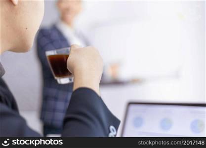 Business partners concept a young male entrepreneur holding a cup of black coffee sitting with a laptop while attending in a monthly meeting.