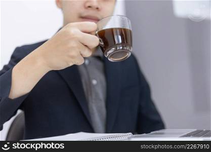 Business partners concept a young male entrepreneur holding a cup of black coffee sitting with a laptop while attending in a monthly meeting.