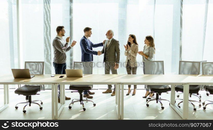 Business partners handshaking in the office after making agreement with employees near by