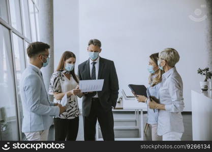 Business partners standing and looking at business results in the office while wearing face masks sa an virus protection