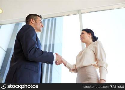 business, partnership and people concept - smiling man and woman shaking hands at office. smiling business people shaking hands at office