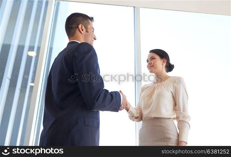 business, partnership and people concept - smiling man and woman shaking hands at office. smiling business people shaking hands at office