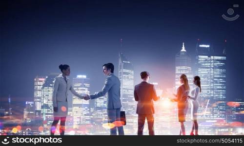 Business partnership as concept. Concept of partnership with business people shaking hands against night city view