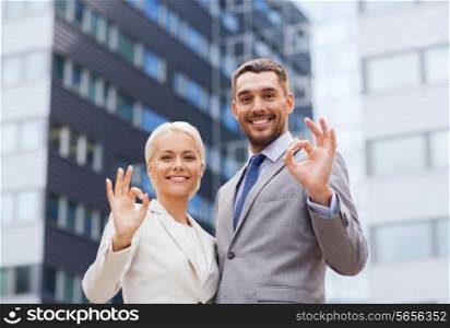 business, partnership, gesture success and people concept - smiling businessman and businesswoman making ok gesture over office building