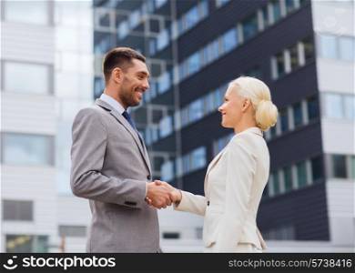 business, partnership, gesture success and people concept - smiling businessman and businesswoman shaking hands over office building
