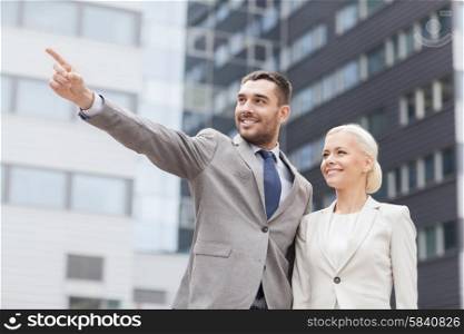 business, partnership, gesture success and people concept - smiling businessman and businesswoman pointing finger over office building
