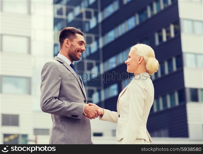 business, partnership, gesture success and people concept - smiling businessman and businesswoman shaking hands over office building