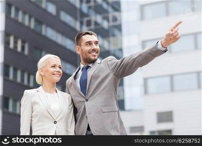 business, partnership, gesture success and people concept - smiling businessman and businesswoman pointing finger over office building