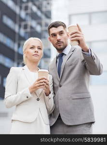 business, partnership, hot drinks and people concept - serious businessmen with paper cups standing over office building