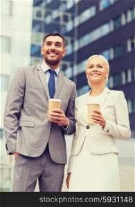 business, partnership, hot drinks and people concept - smiling businessmen with paper cups standing over office building