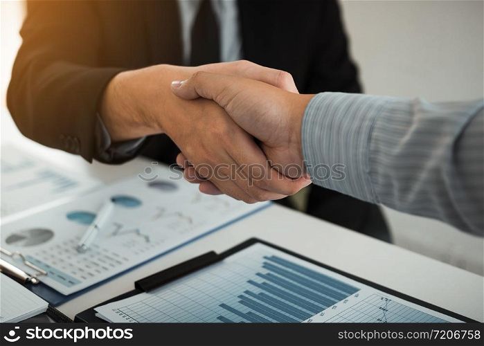 Business partnership shaking hands for signing company financial statements report and profits earned during years in office room.