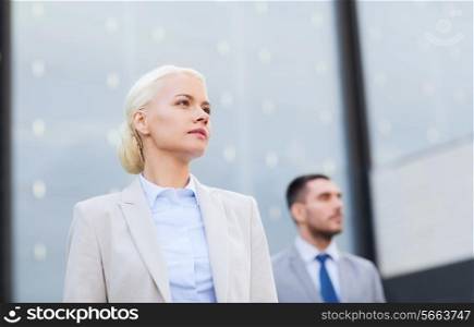 business, partnership, success and people concept - close up of serious businessman and businesswoman standing over office building
